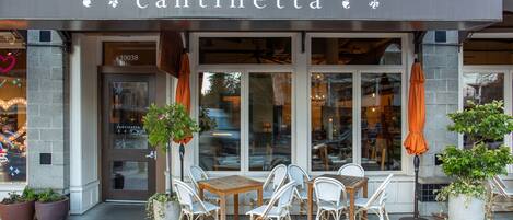 A storefront with the name "cantinetta" above the entrance, featuring a brick-paved patio with outdoor seating and potted plants.