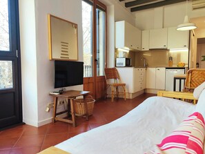 Una camera da letto con un letto, TV, scrivania, sedia e angolo cottura con mobili e lavello.