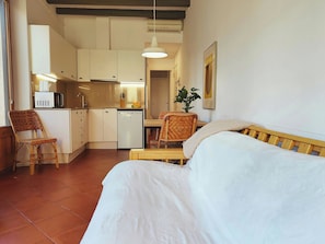 Ein kleines Zimmer mit Bett, Esstisch, Küchenzeile und einem Stuhl.