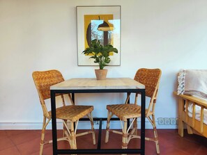 Zona pranzo con tavolo, quattro sedie in vimini, una pianta in vaso e un quadro appeso al muro.