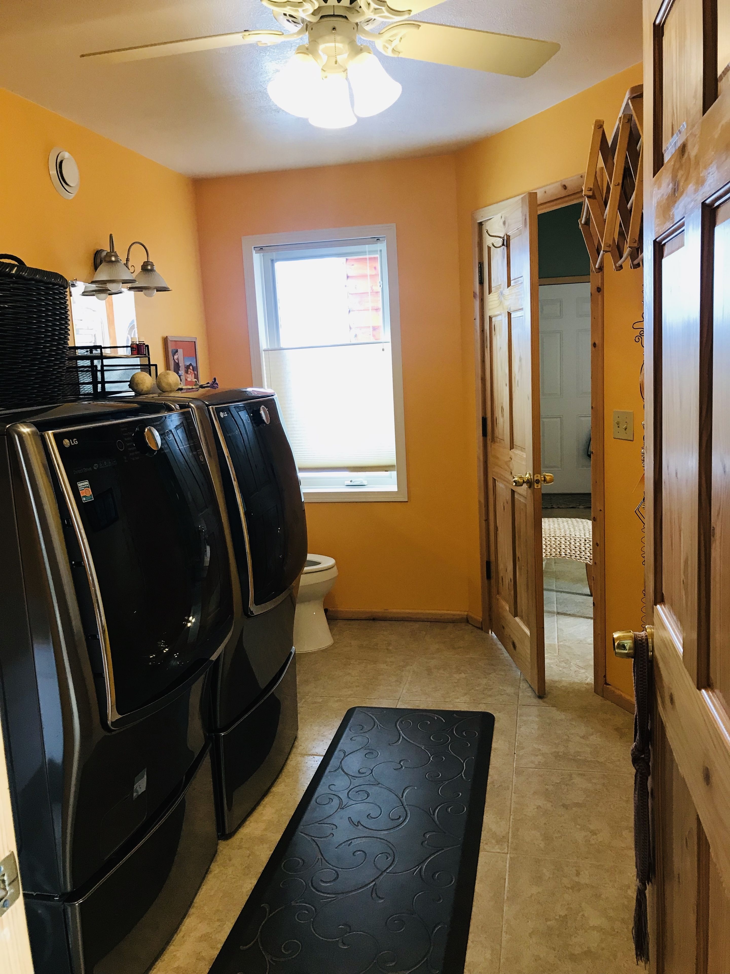 Un lavadero con dos lavadoras y secadoras LG, una ventana, una puerta que da a otra habitación y un ventilador de techo.
