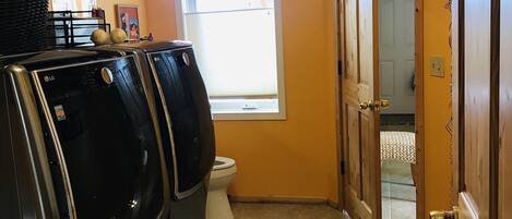 Un lavadero con dos lavadoras y secadoras LG, una ventana, una puerta que da a otra habitación y un ventilador de techo.