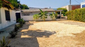 A courtyard with a gravel path, a small garden with banana plants, and a building with a tiled roof. - Oasis de Tolú Hostel, Studio Apartment 101, basic accommodations for a great stay (Santiago de Tolú)