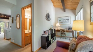 Una sala de estar acogedora con techo de madera, una estantería, un escritorio con lámpara y un cuadro en la pared.