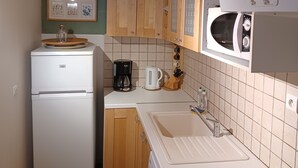Eine kompakte Küche mit Kühlschrank, Mikrowelle, Kaffeemaschine und Waschmaschine.