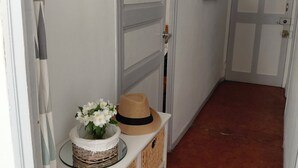 Ein Flur mit einer weißen Tür, einem Spiegel und einem Korbwagen mit Blumen.