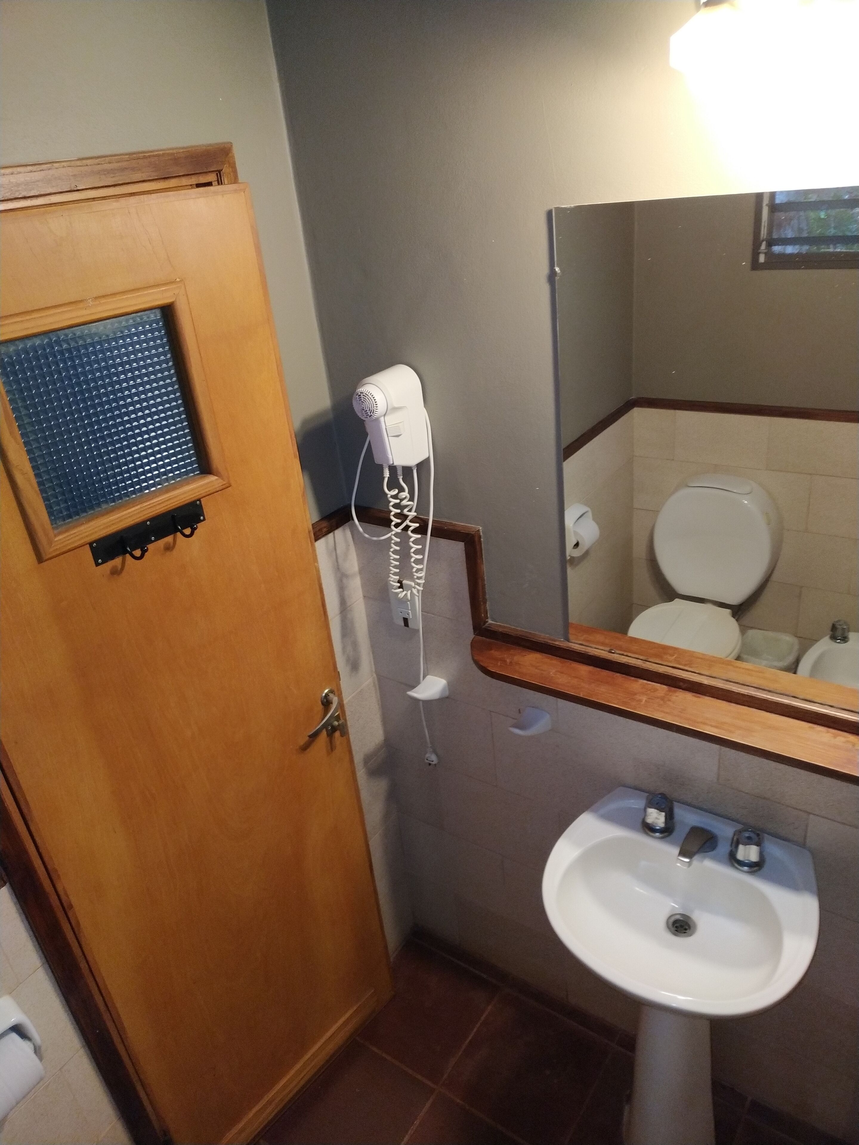A bathroom with a wooden door, a white sink, a mirror, and a hairdryer mounted on the wall.