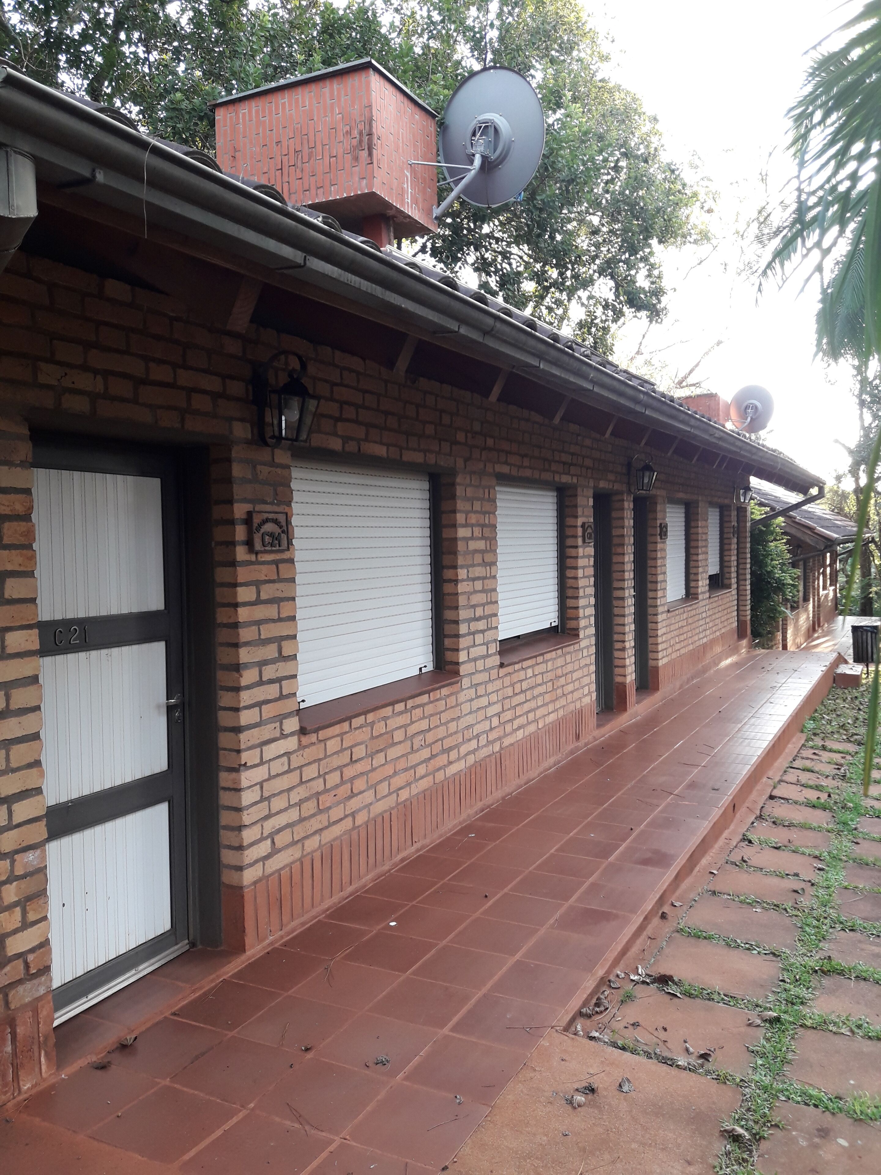 Un edificio de ladrillo con ventanas a la francesa cerradas, una antena parabólica y un camino empedrado.