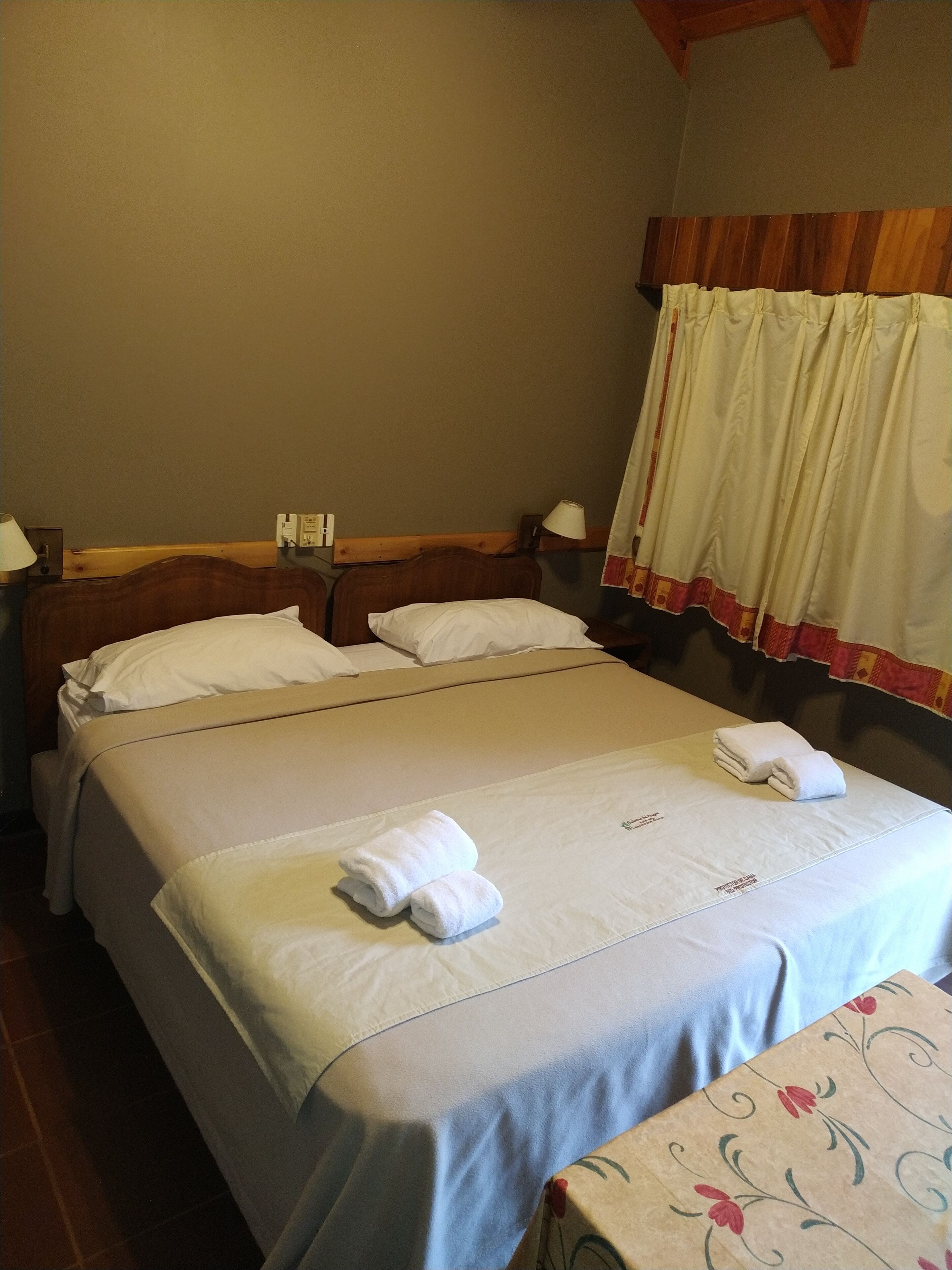 Ein Hotelzimmer mit einem großen Bett, zwei Nachttischen, einem Fenster mit Vorhängen.