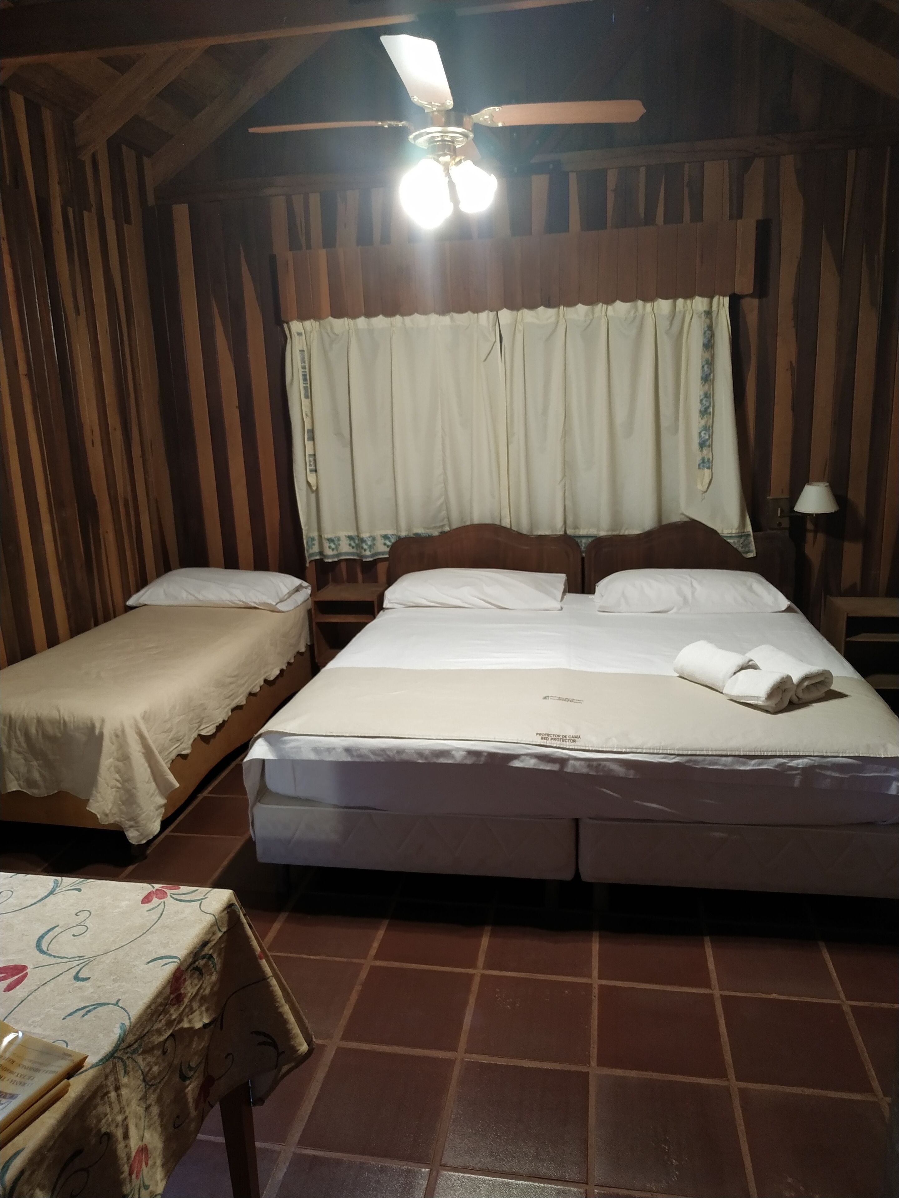 A room with two beds, a ceiling fan, and a table with a floral tablecloth.