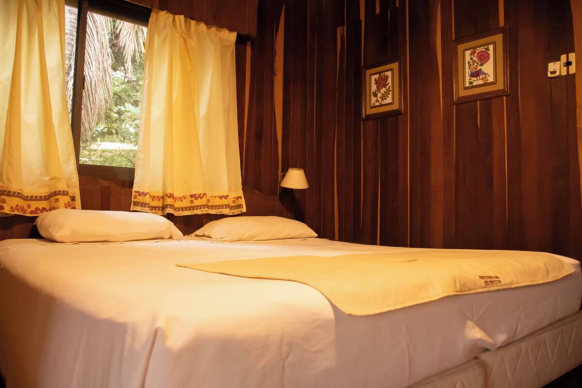 A bed with white linens, a bedside lamp, and a window with curtains.
