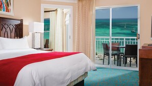 A hotel room with a large bed, a desk, and a view of the ocean through a sliding glass door.