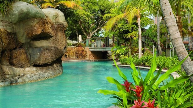 A pool surrounded by tropical vegetation and a rock formation.