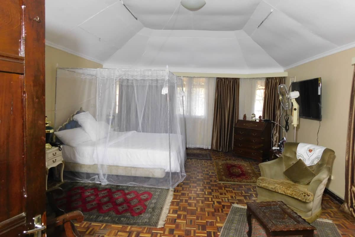 A bedroom with a bed under a mosquito net, a wooden dresser, a television on the wall, and a patterned rug.