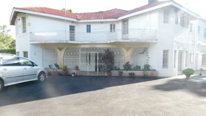 Un edificio de dos pisos con techo de tejas rojas, entrada con reja y macetas con plantas a lo largo de la fachada.