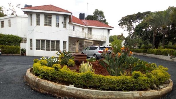 Un edificio blanco con tejado rojo, rodeado por un jardín ajardinado con diversas plantas y flores.
