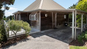 A modern building with a sloped roof, a covered porch, and a concrete walkway leading to the entrance. - Te Maiki Escape - Russell Holiday Home (Russell)
