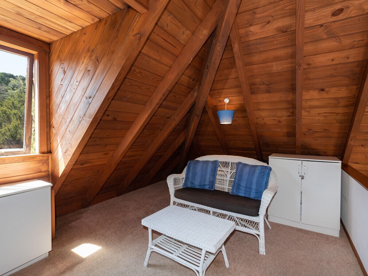 A cozy attic bedroom with a wooden ceiling, a white sofa with blue cushions, a small white table, and a white cabinet.