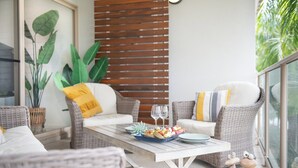 Un balcone con mobili in vimini, un tavolo da pranzo con una ciotola di frutta e delle figure decorative a forma di rana.