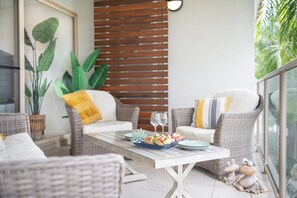 A balcony with wicker furniture, a dining table with a fruit bowl, and decorative frog figures. - Phil's Place on Airlie (Airlie Beach)