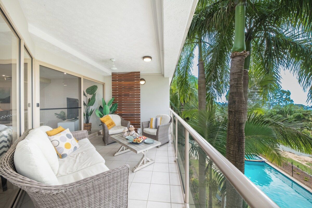 A balcony with wicker furniture, a pool, and a view of palm trees.