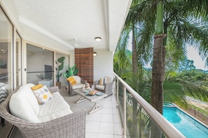Un balcón con mobiliario de mimbre, una piscina y vistas a palmeras.