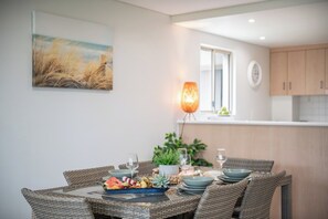 A dining area with wicker furniture, a table set with plates, glasses, and a centerpiece. - Phil's Place on Airlie (Airlie Beach)