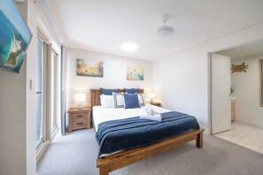 A bedroom with a bed, bedside tables, and artwork on the walls. - Phil's Place on Airlie (Airlie Beach)