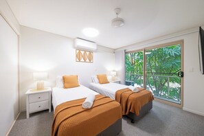 Ett hotellrum med två sängar, ett fönster med utsikt över grönområden, en takfläkt och en luftkonditioneringsanläggning.
