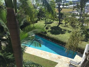 A swimming pool surrounded by palm trees and a grassy area. - Phil's Place on Airlie (Airlie Beach)