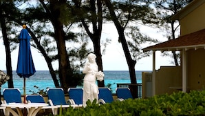 Eine Statue einer Frau, die ein Blumenstrauß und einen blauen Regenschirm hält, mit Poolanlage, Liegestühlen und Blick auf den Ozean.