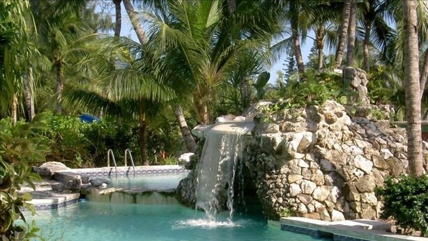 Ein Pool mit Wasserfall, umgeben von Palmen und Felsen.