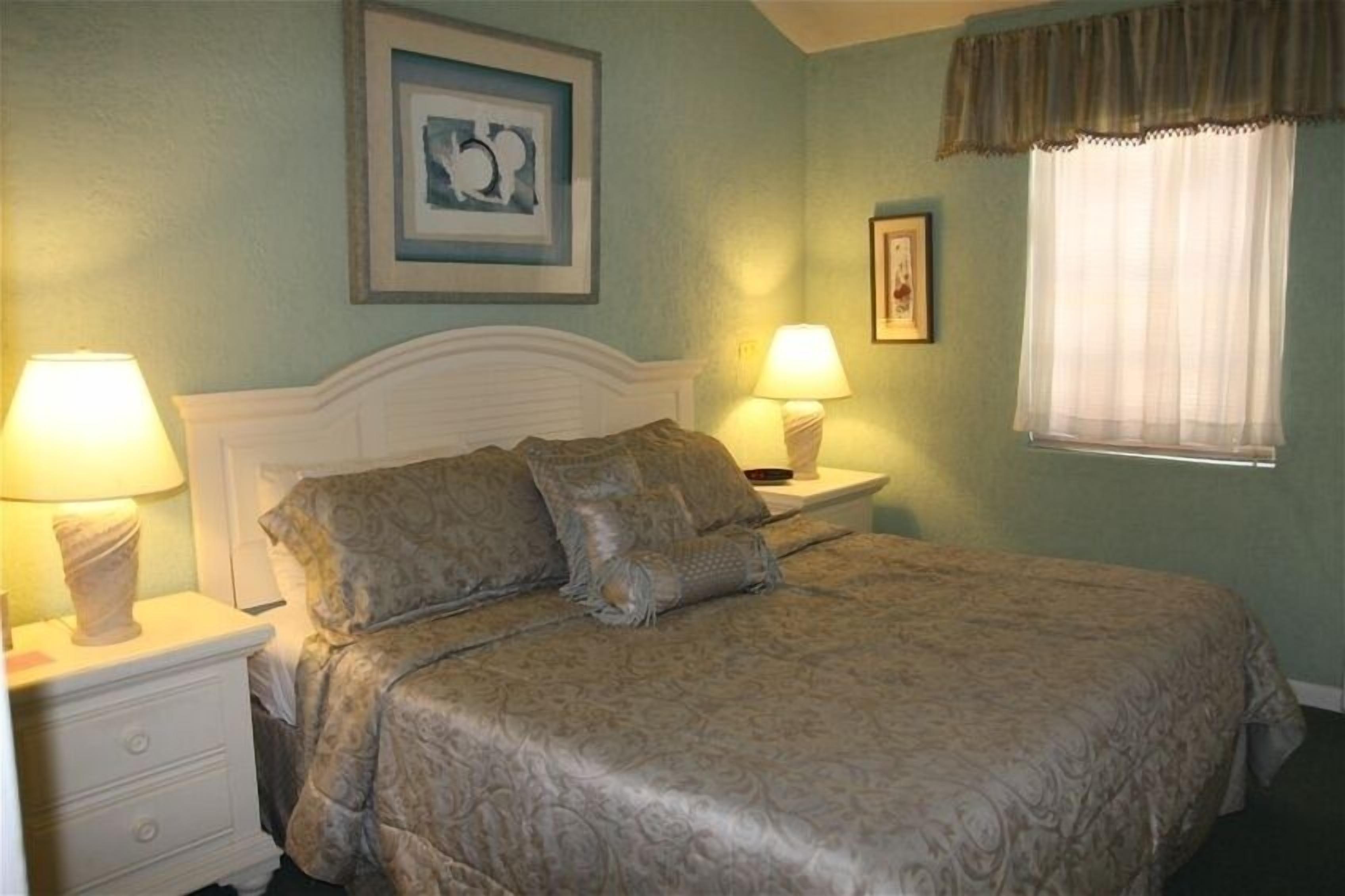 A bedroom with a large bed, two bedside tables with lamps, a framed picture on the wall, and a window with a curtain.