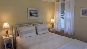 Een net opgemaakt bed met witte lakens, twee bedlampjes en een lijst met een afbeelding aan de muur.