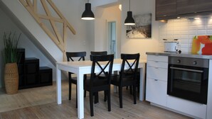 Una cocina moderna con una mesa blanca, sillas negras, una escalera de madera y un ventanal grande.