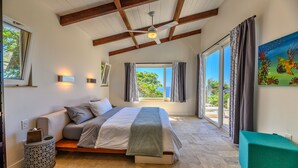 A bedroom with a bed, a bedside table, a window, and a view of the outdoors. - Villa Topaz Guest Villa Above West Bay With 180 Degree Views @ Villa Topaz (West Bay)