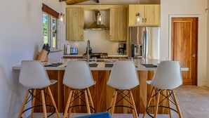 A modern kitchen with wooden cabinets, a stainless steel refrigerator, and a central island with bar stools. - Villa Topaz Guest Villa Above West Bay With 180 Degree Views @ Villa Topaz (West Bay)