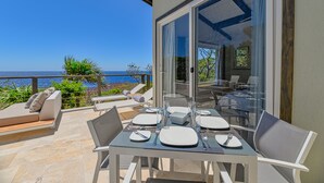 A terrace with a table set for dining, overlooking a scenic view of the sea. - Villa Topaz Guest Villa Above West Bay With 180 Degree Views @ Villa Topaz (West Bay)