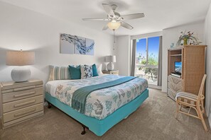 A bedroom with a bed, dresser, nightstands, a ceiling fan, artwork, and a view through a window.