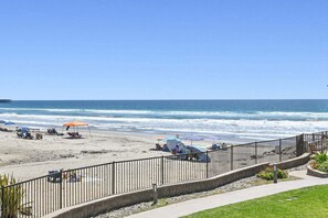 Ein Strand mit Zaun, Sonnenschirmen und Liegestühlen.