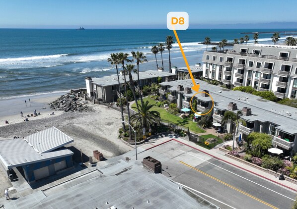 An aerial view of a coastal hotel with a parking lot, beach access, and ocean views.
