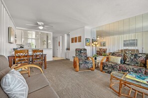 A spacious living room with a sofa, chairs, a dining table, and a kitchen area visible through an open door. - Charming Upper Beachfront Cottage-Breathtaking Ocean Views-D8 North Coast Village (Oceanside)