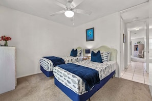 A bedroom with two beds, a ceiling fan, a framed picture on the wall, and a hallway leading to another room. - Charming Upper Beachfront Cottage-Breathtaking Ocean Views-D8 North Coast Village (Oceanside)