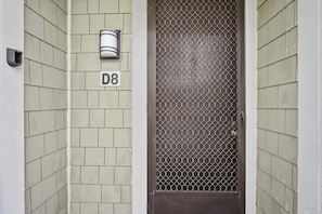 Een deur met een gaasraam, een lamp erboven en een huisnummer 'D8' op de muur.