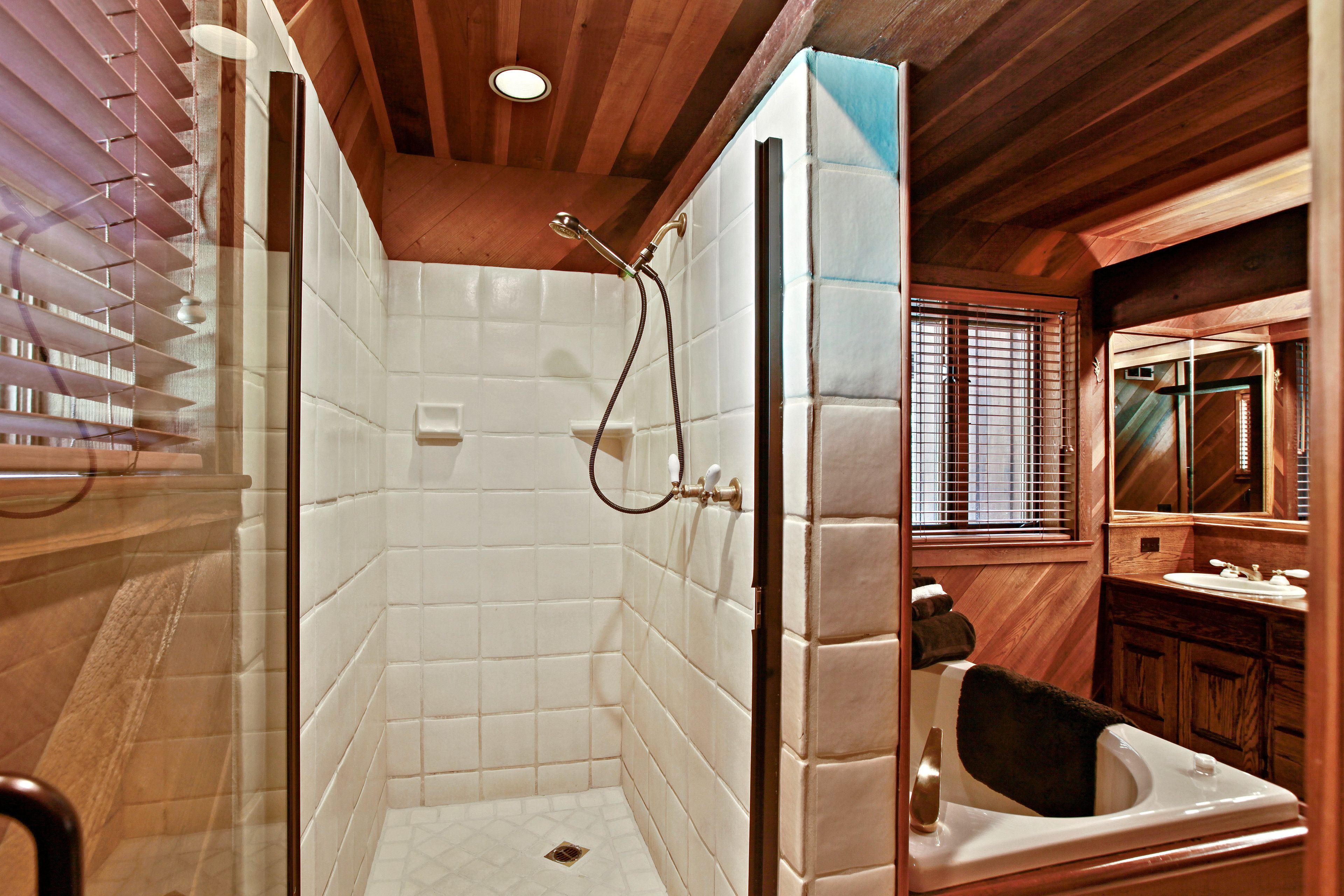 A bathroom with a shower, toilet, and sink, featuring wooden paneling and a tiled floor.