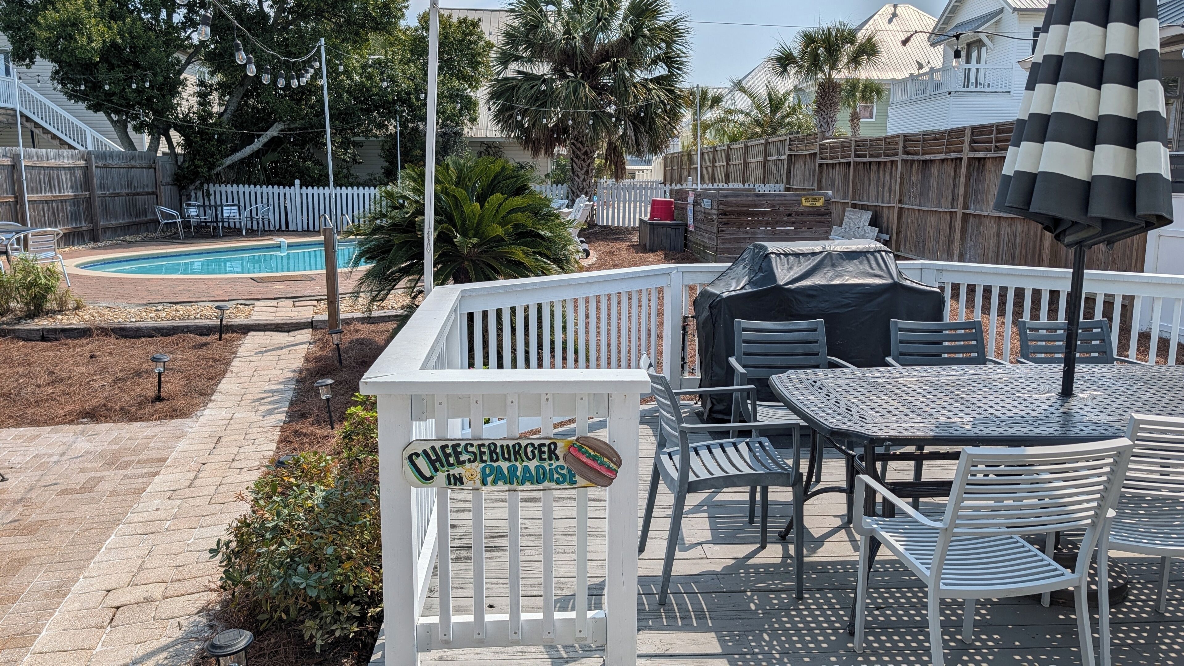 Una terraza con un cartel que dice 'CHEESEBURGER IN PARADISE', muebles de exterior y una piscina al fondo.