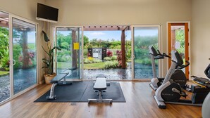 Ruime kamer met een grote schuifglazen deur naar een tuin, voorzien van een loopband, elliptische trainer en een bankje.
