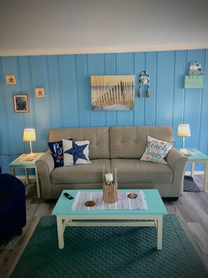 A living room with a beige sofa, two side tables with lamps, a coffee table with a candle, and a blue wall with vertical lines and decorations. - Downtown OC, Water views!  (Ocean City)