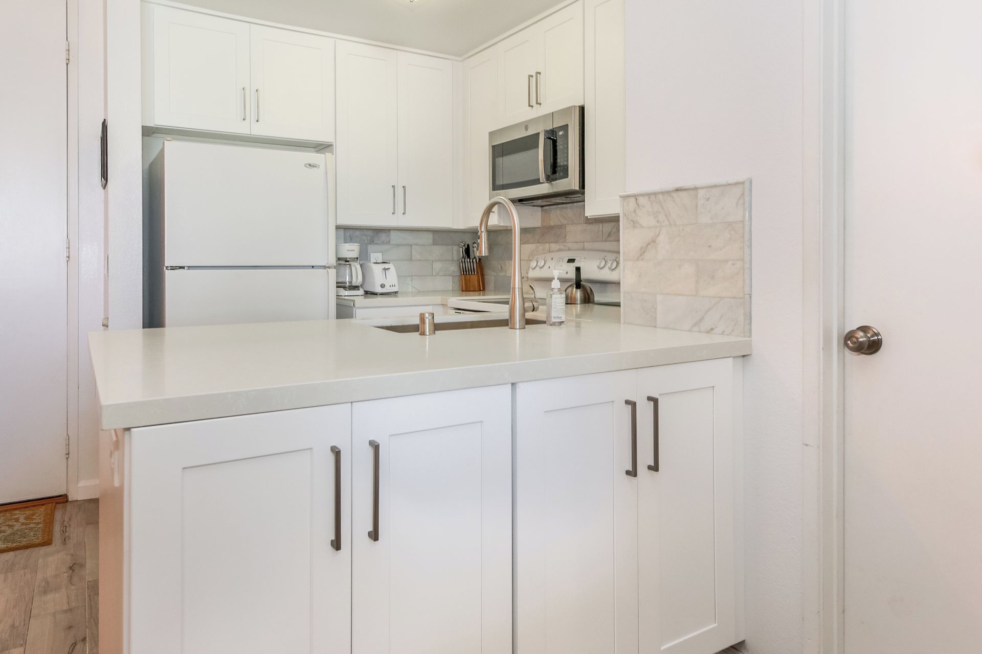 A modern kitchen with white cabinetry, stainless steel appliances, and a marble backsplash.