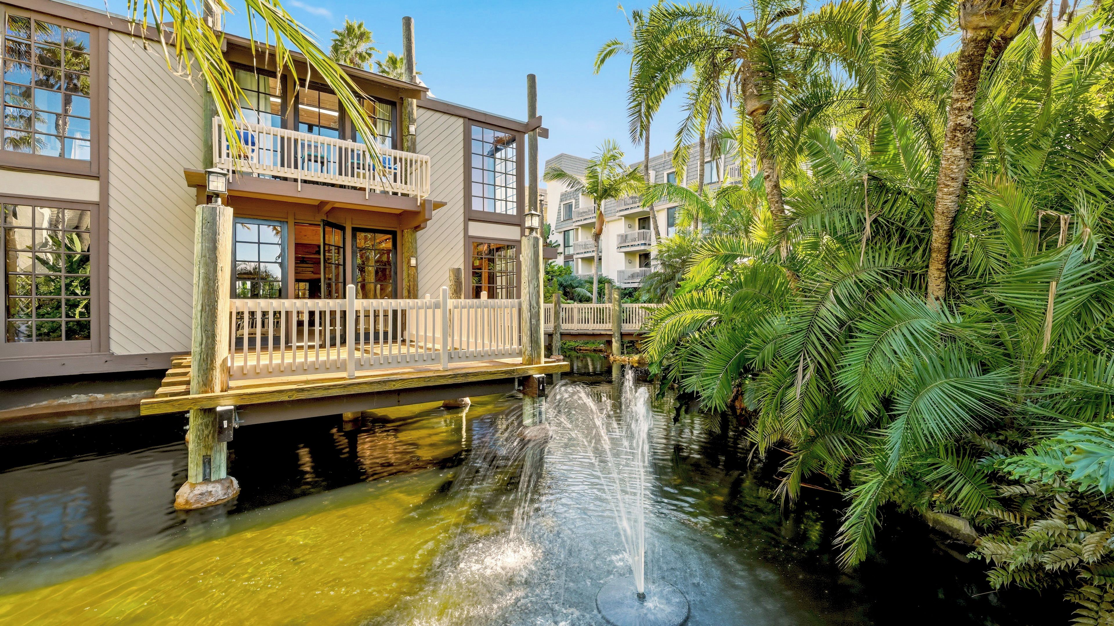 A waterfront hotel with a balcony, a water feature, and lush greenery.